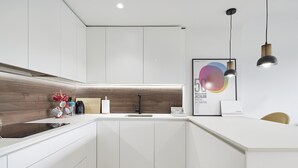 A modern kitchen with white cabinets, a wooden backsplash, and a black faucet. There is a framed artwork on the wall and a coffee machine on the counter. - COMFORTABLE AND BRAND NEW APARTMENT (Zarautz)