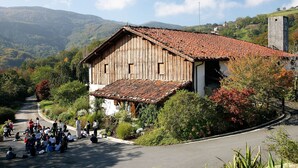 A rustic wooden building with a red-tiled roof, surrounded by lush greenery and a winding road. - COMFORTABLE AND BRAND NEW APARTMENT (Zarautz)