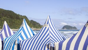 Beach umbrellas with a striped pattern, a coastal view with waves, and a forested hill in the background. - COMFORTABLE AND BRAND NEW APARTMENT (Zarautz)