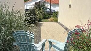 Une terrasse avec deux chaises bleu clair, un espace recouvert de gravier et une maison en arrière-plan.