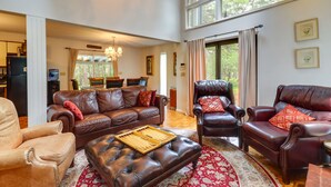 A spacious living room with leather sofas, a coffee table, and a chandelier. - Fire Pit, Kayaks & Hammocks: Long Pond Home! (Long Pond)
