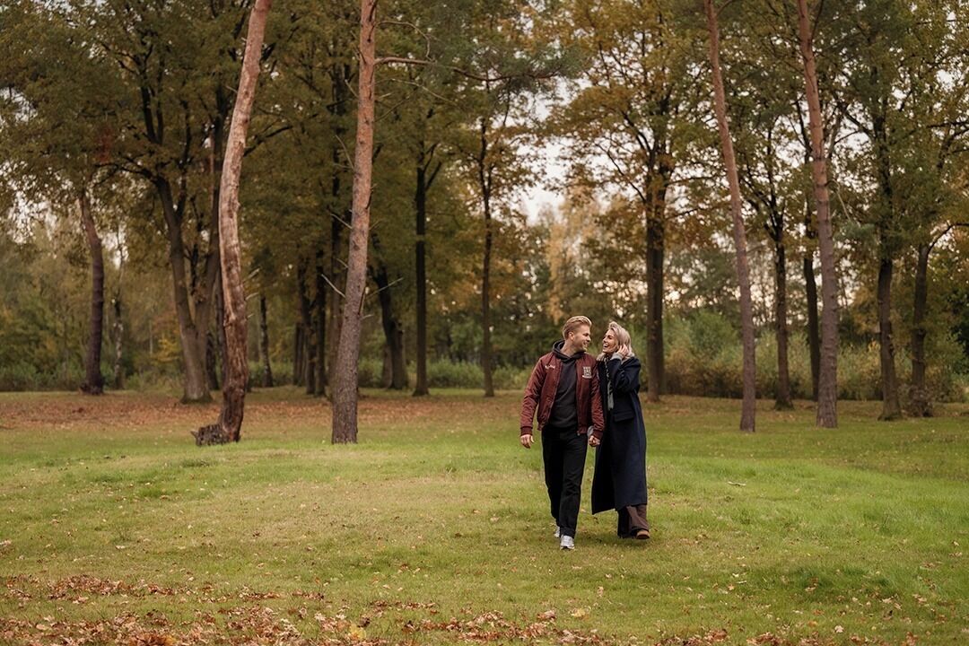 Un couple se promène dans un parc verdoyant, bordé d’arbres.