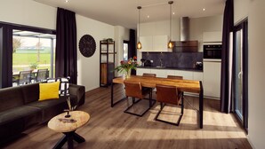 A modern kitchen with a dining area, a sofa with yellow cushions, and a wooden coffee table. -  Hofparken De Bergvennen  (Lattrop)