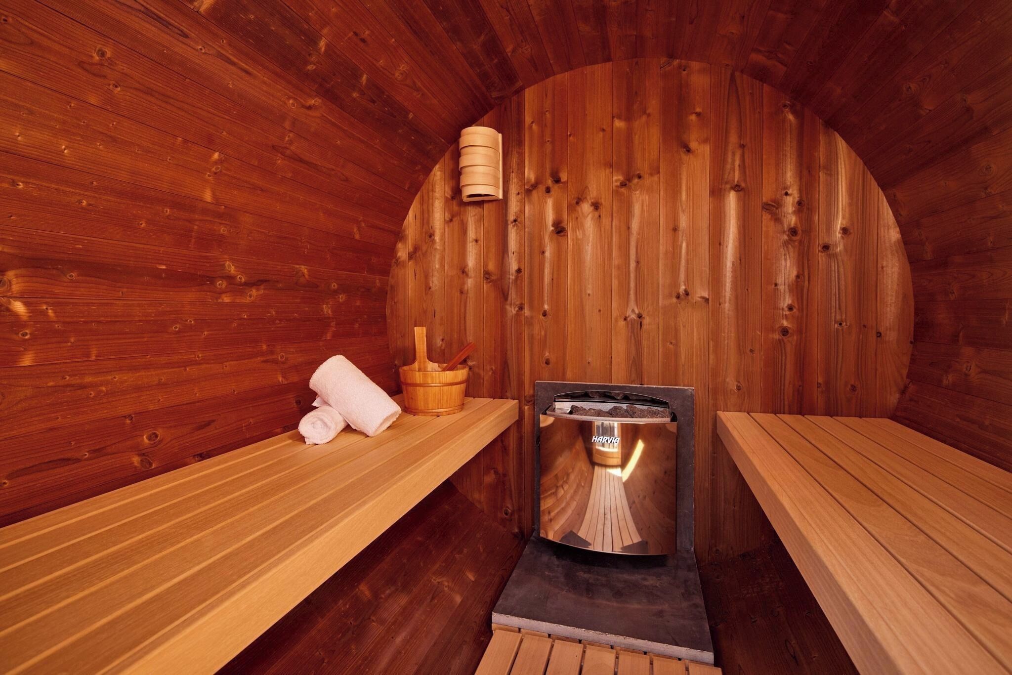 A sauna room with wooden walls, benches, a sauna heater, and a wooden bucket.