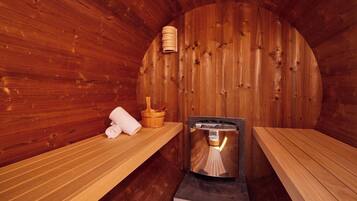 A sauna room with wooden walls, benches, a sauna heater, and a wooden bucket.