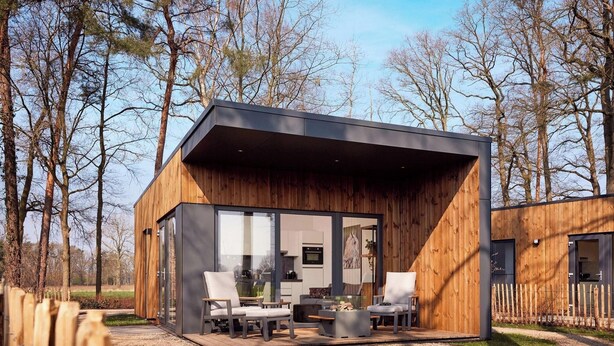 A modern wooden cabin with a glass door, outdoor seating, and a view of the surrounding trees. -  Hofparken De Bergvennen  (Lattrop)