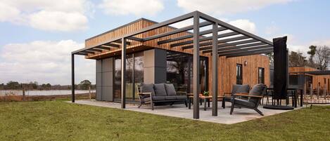 A modern outdoor living space with a wooden pergola, a sofa, and two chairs.