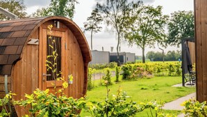 A wooden cabin with a curved roof, surrounded by a well-maintained garden and trees. -  Hofparken De Bergvennen  (Lattrop)