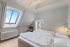 Un dormitorio con techo inclinado, un ventanal grande, un radiador y una cama con ropa blanca.