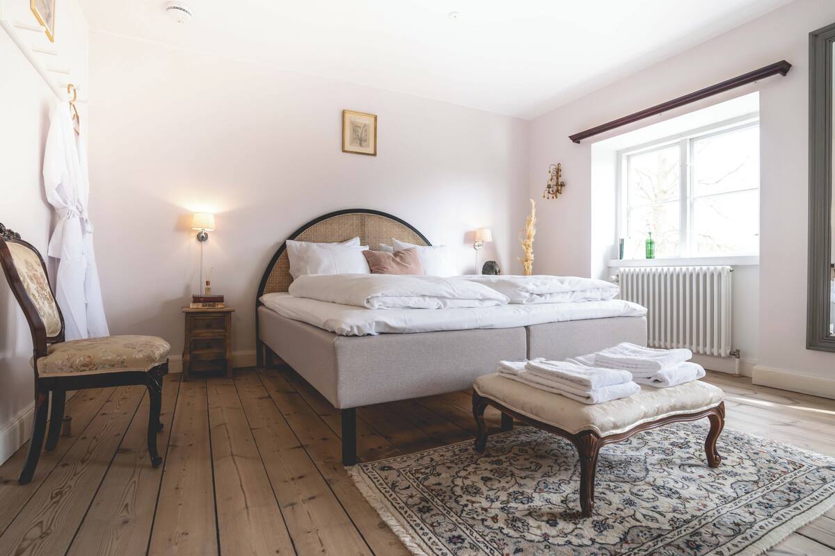 A bedroom with a bed, bedside tables, a chair, a window, and a radiator.