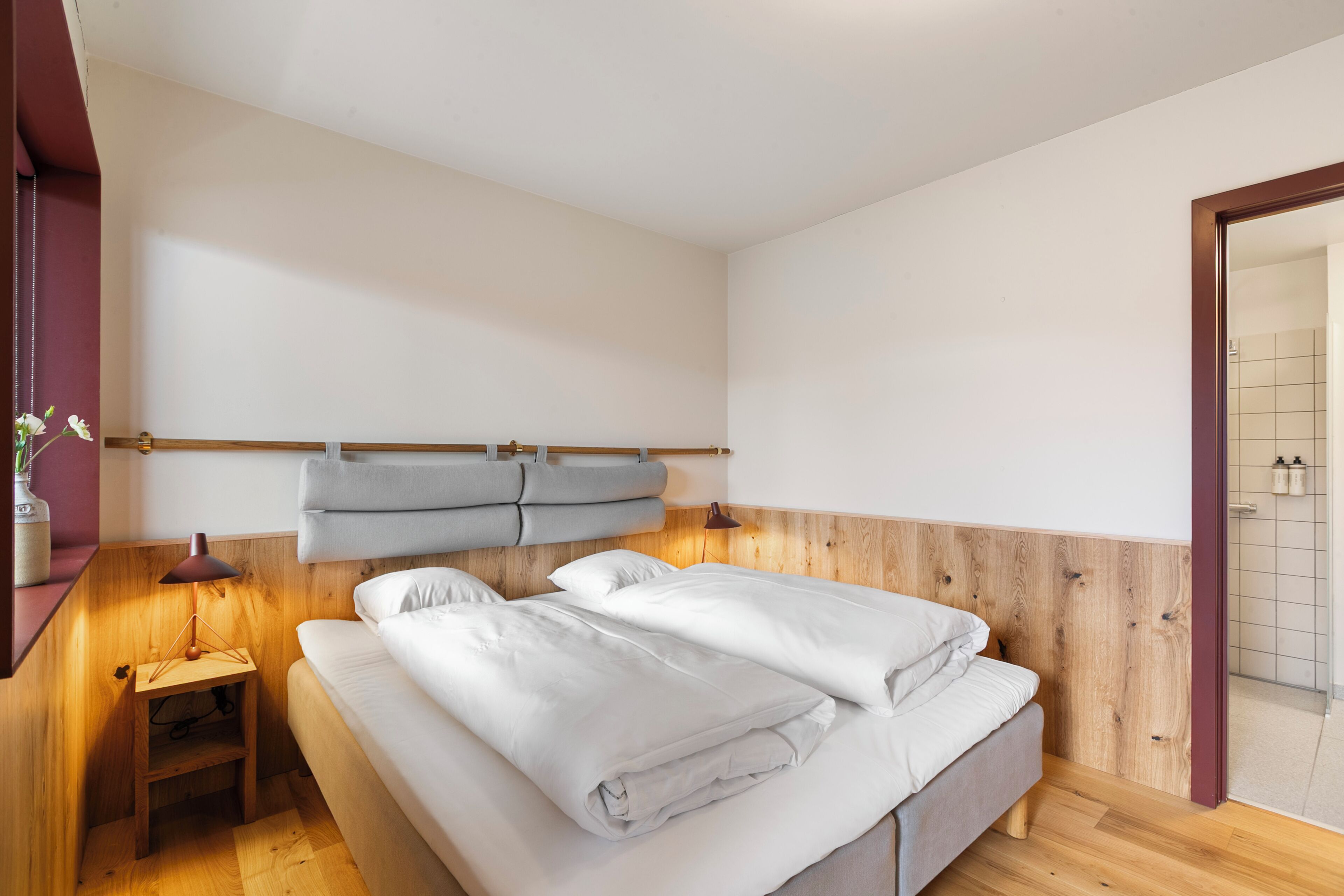 Een slaapkamer met een bed, nachtkastje, lamp en een houten hoofdbord.
