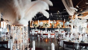 Un salón de banquetes con mesas redondas dispuestas para un evento formal, con manteles blancos, velas y centros de mesa florales.