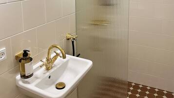 A bathroom with a white sink, gold fixtures, and a shower with a gold showerhead.