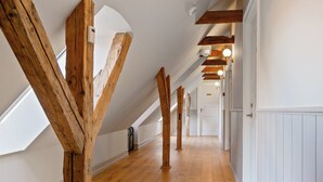 Un pasillo con vigas de madera, paredes blancas y suelo de madera.