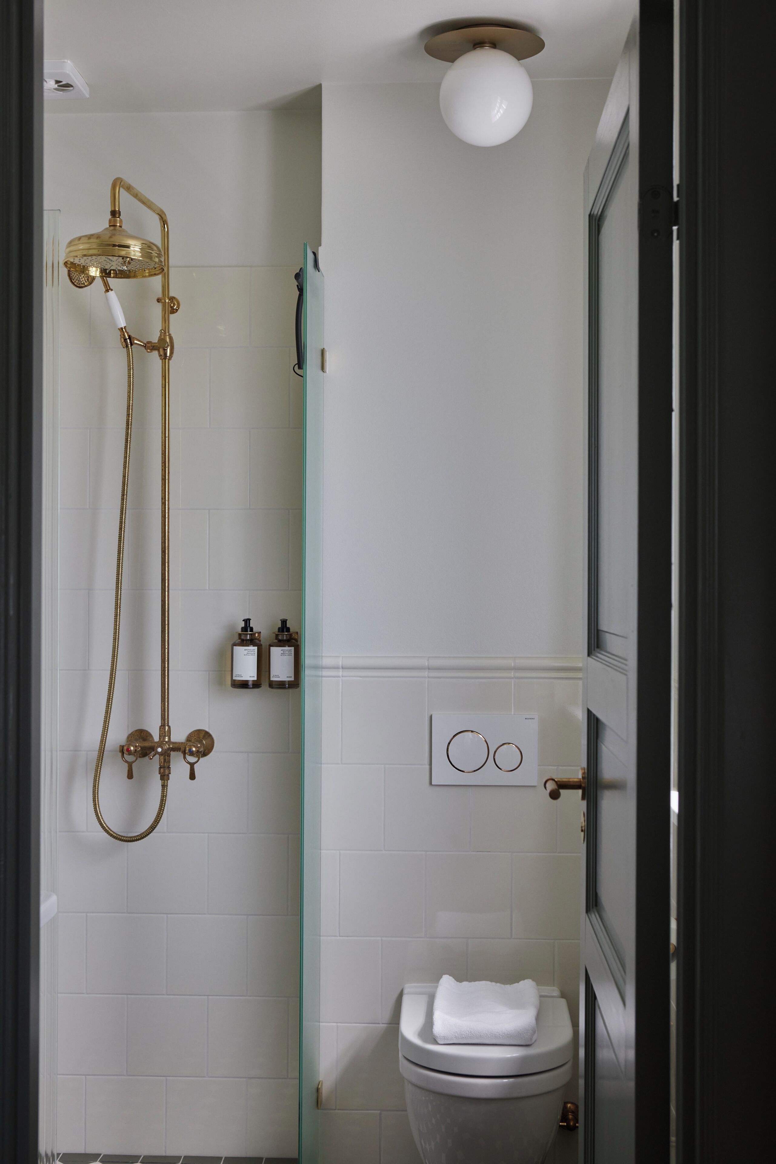 A modern bathroom with a glass shower enclosure, a toilet, and a wall-mounted control panel.