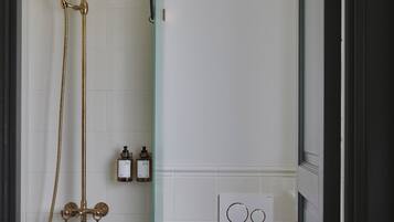 A modern bathroom with a glass shower enclosure, a toilet, and a wall-mounted control panel.