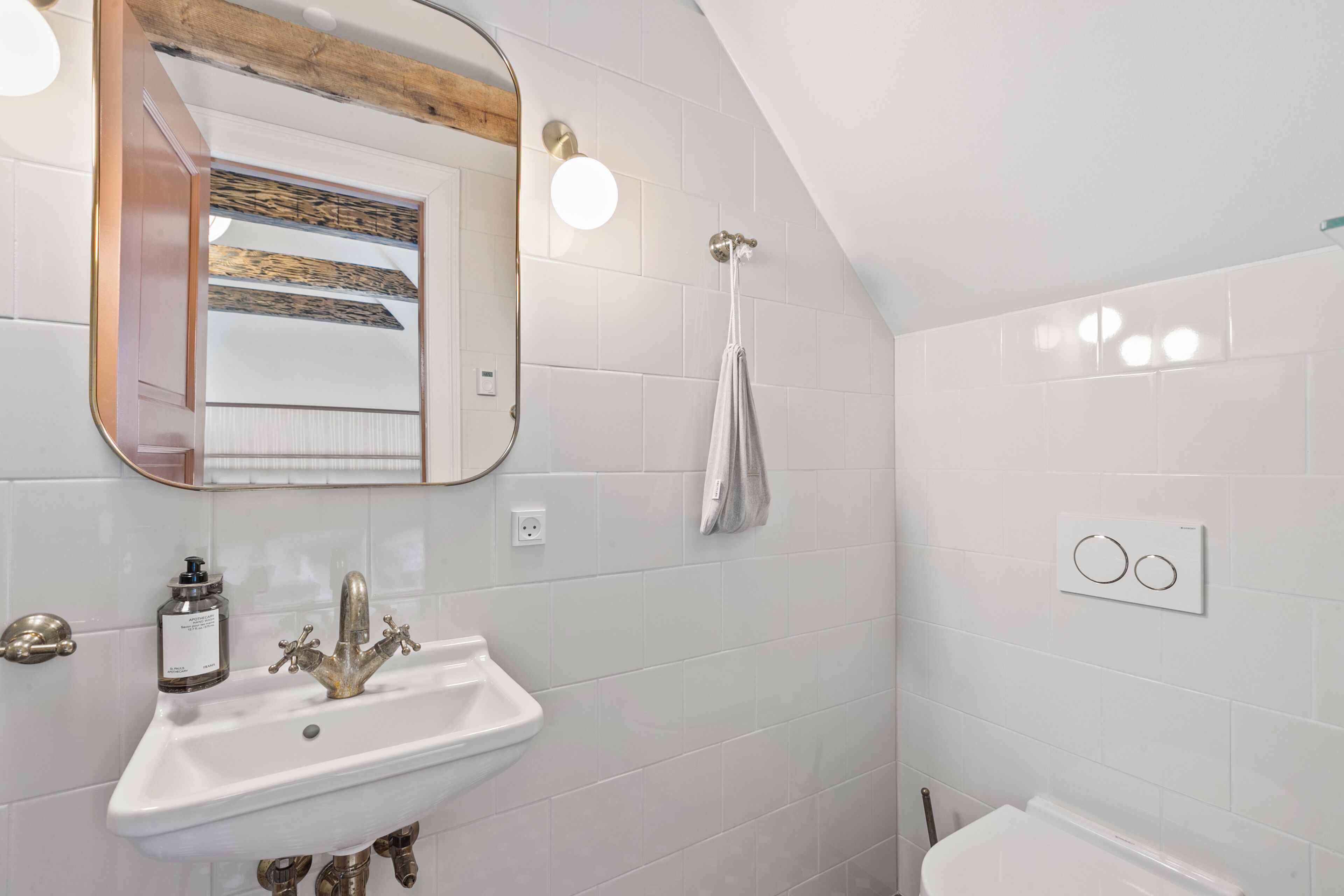A bathroom with a white sink, a mirror with a wooden frame, a towel hanging on a hook, and a shower with a white wall.
