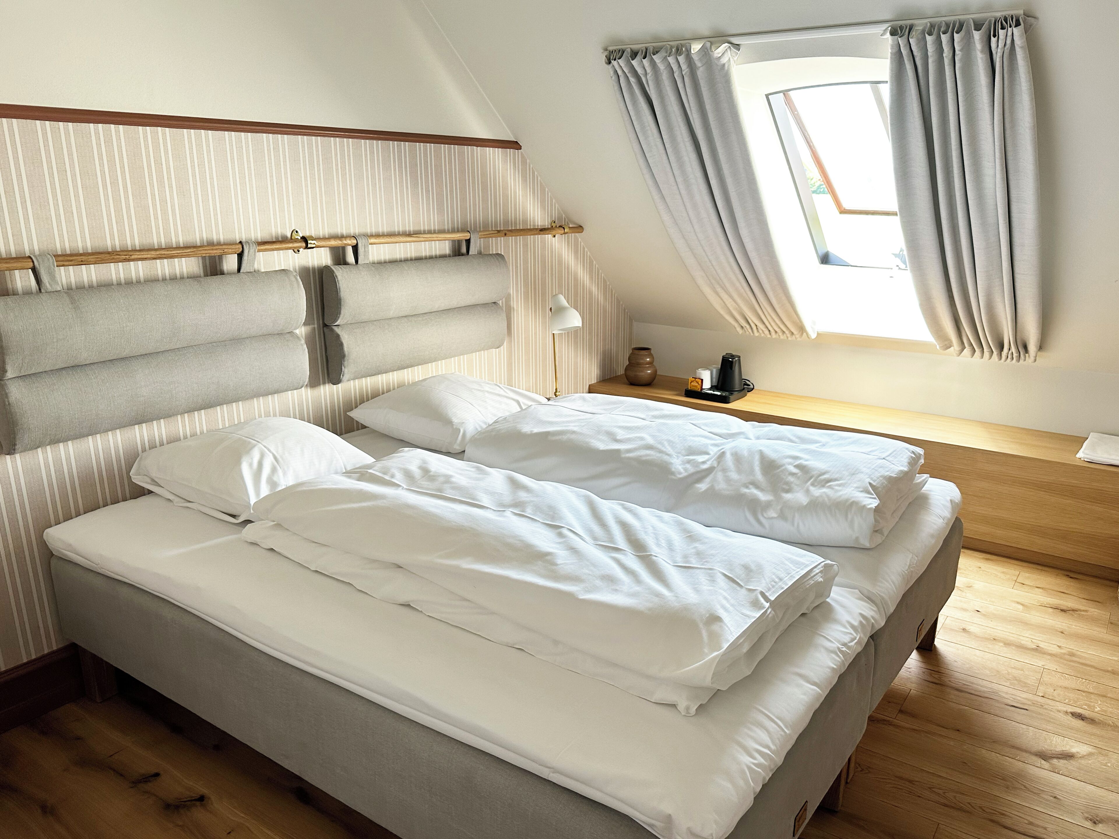 A bedroom with a large bed, a bedside table, a window with curtains, and a striped wall.