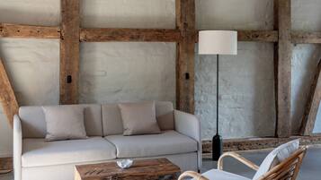 A room with exposed wooden beams, a sofa, a wicker chair, a floor lamp, and a coffee table.