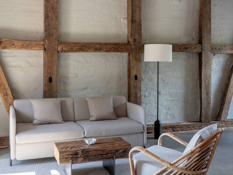A room with exposed wooden beams, a sofa, a wicker chair, a floor lamp, and a coffee table.