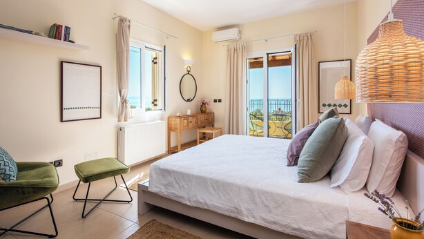 Une chambre à coucher avec un lit, un fauteuil vert, une table de chevet en bois, une fenêtre avec des rideaux et un balcon.