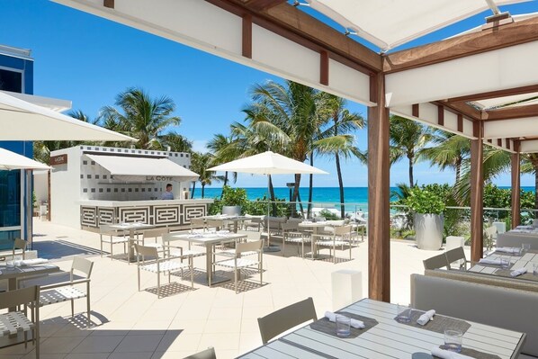 An outdoor dining area with tables and chairs, a bar, and a view of the ocean.