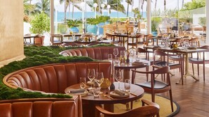 A restaurant with round tables and leather booths, large windows with a view of palm trees and the ocean. - CasaGrandeSouthBeach by AmericanVacationLiving 6BR (Miami Beach)