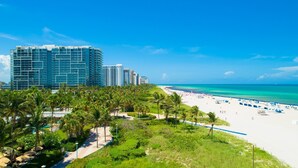 A beach with palm trees, a sandy shore, and a row of high-rise buildings in the background. - CasaGrandeSouthBeach by AmericanVacationLiving 6BR (Miami Beach)