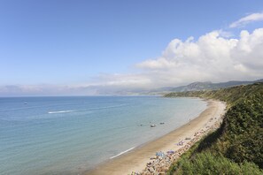 Uma praia costeira com águas cristalinas, areal arenoso e um penhasco rochoso.