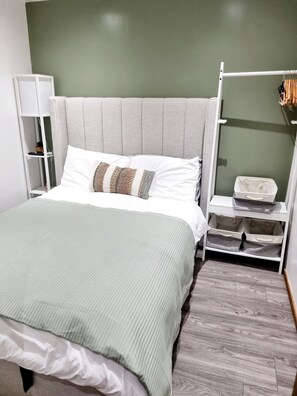 Un dormitorio ordenado con cama, mesita de noche, armario y cajas de almacenamiento.