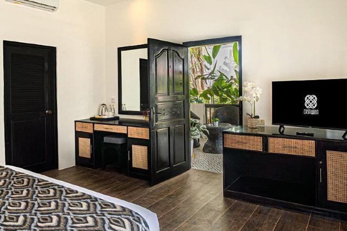 A hotel room with a bed, a dresser, a television, and a door leading to a balcony with a plant.