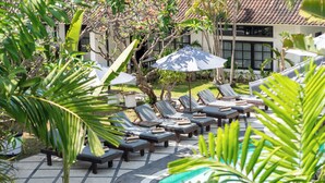 A poolside area with lounge chairs and umbrellas, surrounded by tropical plants. - Casa Wina Kuta (Kuta)
