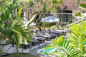 Zona de piscina con sillones reclinables y sombrillas, rodeada de plantas tropicales.