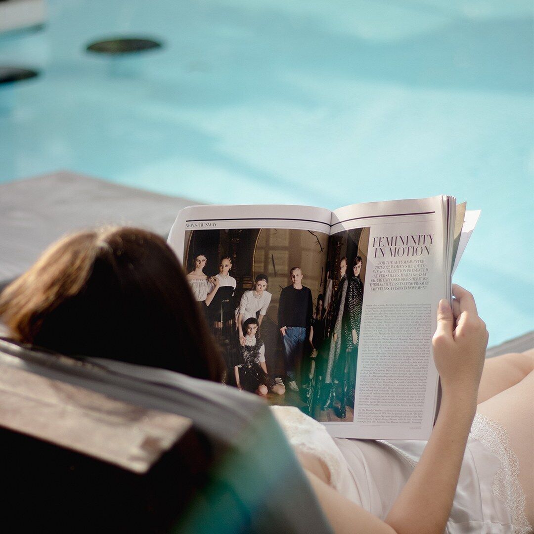 A person lying on a lounge chair by a pool, reading a magazine.