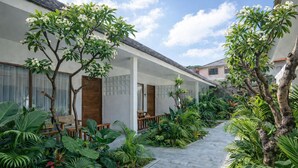 A covered outdoor seating area with wooden furniture, surrounded by lush tropical plants and a paved walkway. - Casa Wina Kuta (Kuta)