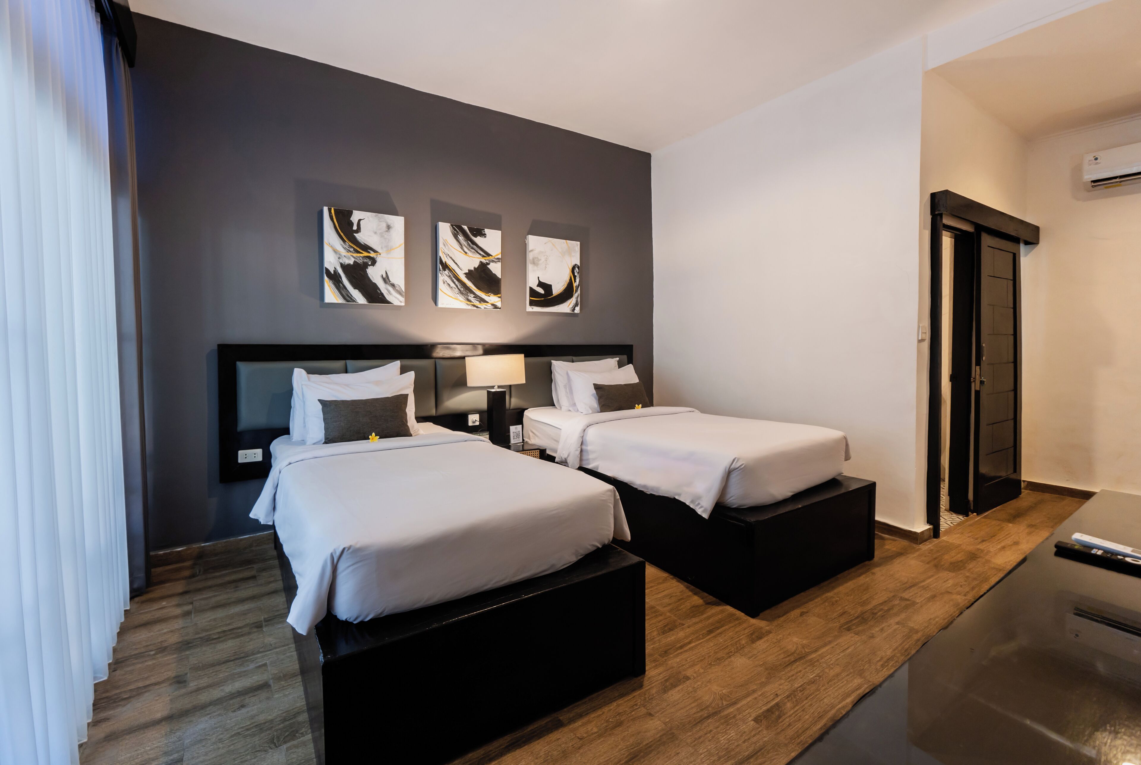 A hotel room with two beds, a dark wall, and three abstract paintings.
