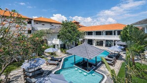 A hotel courtyard with a swimming pool, lounge chairs, and umbrellas. - Casa Wina Kuta (Kuta)