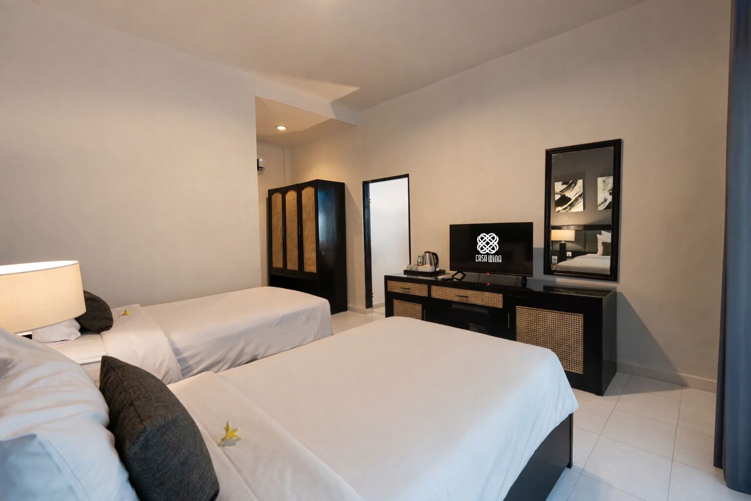 A hotel room with two single beds, a television, a wardrobe, and a mirror.