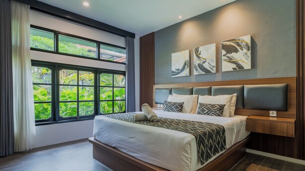 A modern bedroom with a large bed, a view of greenery through large windows, and abstract art on the wall. - Casa Wina Kuta (Kuta)