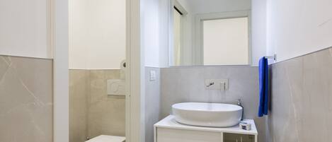 Uma casa de banho moderna com uma pia branca, espelho e sanita.