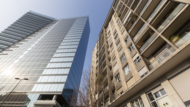 Ein modernes Hochhaus mit Glasfassade und ein angrenzendes, älteres Gebäude mit Balkonen.