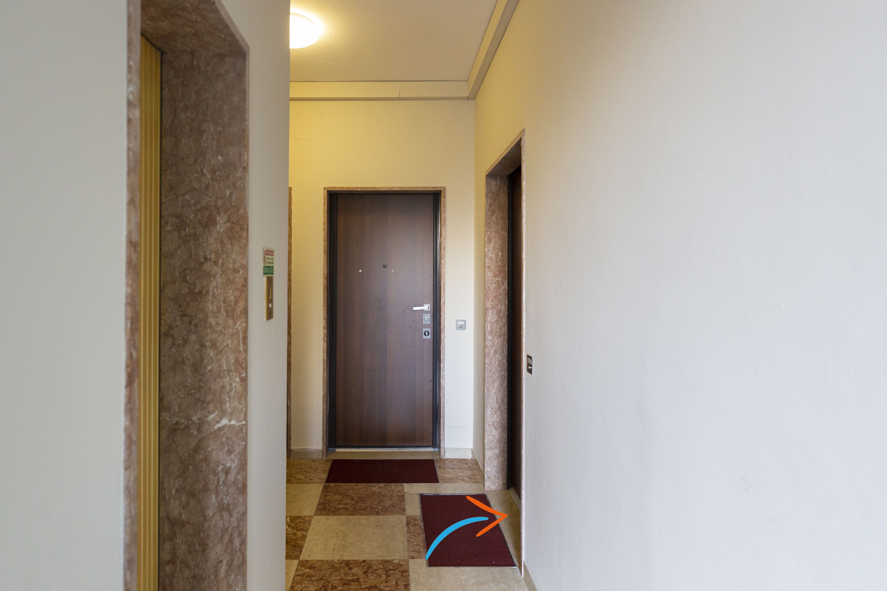 A hallway with a marble floor, a door at the end, and a red carpet leading to it.