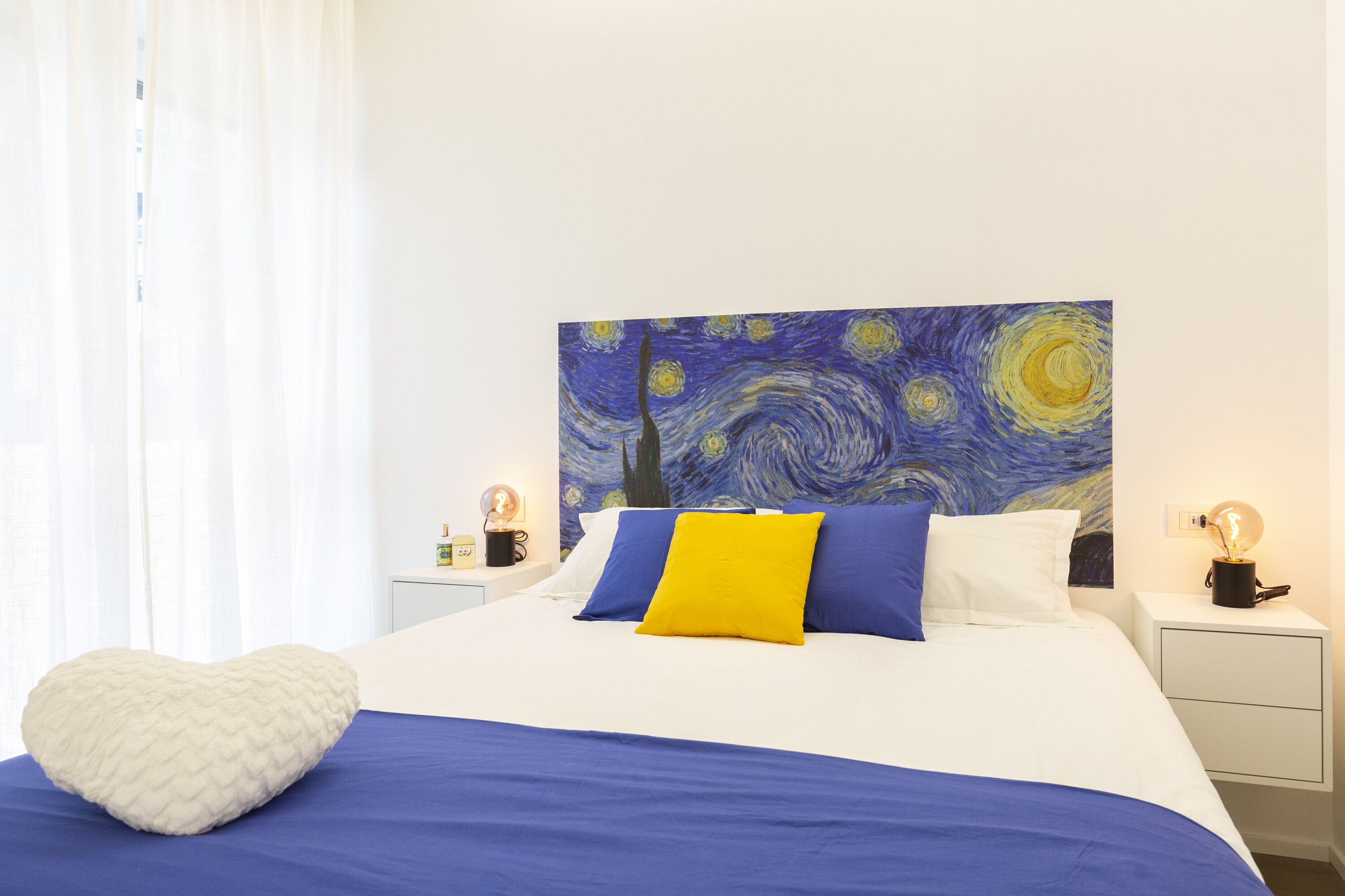 A bedroom with a bed, white nightstands, a white dresser, and a painting on the wall.
