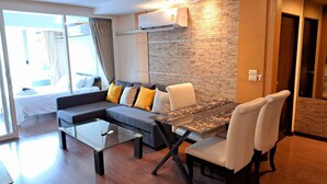 A modern living room with a sofa, a glass coffee table, and a dining table with chairs. - 6D - 3 Bedroom Downtown Apartment With Shared Pool (Bangkok)