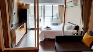 A hotel room with a bed, a sofa, a TV, and a balcony with a view. - 6D - 3 Bedroom Downtown Apartment With Shared Pool (Bangkok)