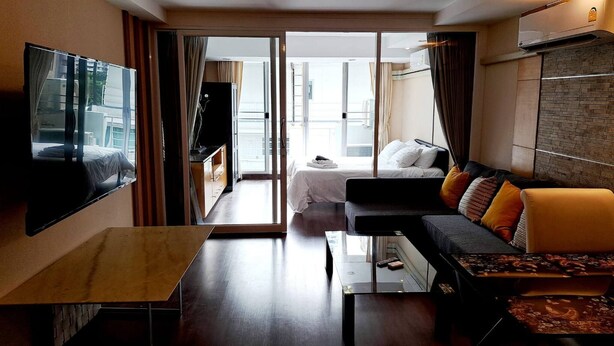 A modern hotel room with a flat-screen TV, a sofa, a bed, and a balcony with curtains. - 6D - 3 Bedroom Downtown Apartment With Shared Pool (Bangkok)