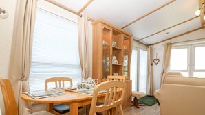 A cozy living area with a wooden dining table, chairs, a sofa, and a cabinet with glass doors. - Gwel Y Môr (Caernarfon)