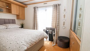 A bedroom with a bed, a wardrobe, a small stool, and a window with curtains. - Gwel Y Môr (Caernarfon)