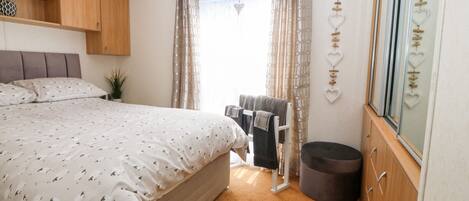 A bedroom with a bed, a wardrobe, a small stool, and a window with curtains.