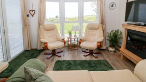 A cozy living room with two armchairs, a green sofa, a fireplace, and a television. - Gwel Y Môr (Caernarfon)